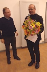 Zwei Herren, einer mit Blumenstrauß und Mikrofon in der Hand